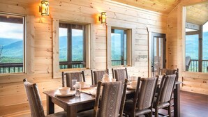 Eine Holzhütte mit Esstisch für sechs Personen, großen Fenstern und Blick auf die Berge.