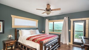 Ein Schlafzimmer mit einem hölzernen Bett, einem Deckenventilator, einem Fenster mit Vorhängen und Blick ins Freie.