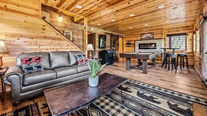 Interior de cabana de madeira com sofá, mesa de centro, lareira e mesa de bilhar.