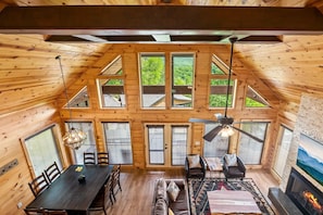 A wooden cabin interior with a dining area, sofa, fireplace, and large windows. - Tennessee Roots (Gatlinburg)