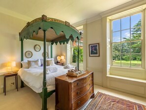 A four-poster bed with a green canopy, a wooden dresser, a window with a view of greenery, and a framed picture on the wall. - Inglethorpe Hall - Nine Bedroom Villa, Sleeps 20 (Ingoldisthorpe)