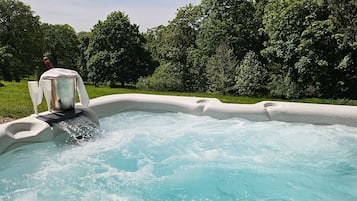 A hot tub with a pump and two glasses, surrounded by a stone border and lush greenery.