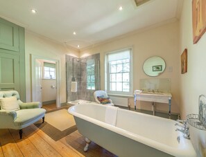 Une salle de bain avec une baignoire sur pieds, un lavabo avec un miroir et une chaise.