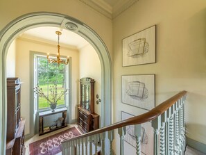 A grand hallway with a chandelier, a wooden console table, a large window with a view, and a staircase with a wooden handrail. - Inglethorpe Hall - Nine Bedroom Villa, Sleeps 20 (Ingoldisthorpe)