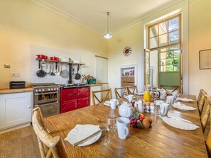 Ein Essbereich mit einem Holztisch, gedeckt für das Frühstück, eine Küche mit roten Schränken und ein großes Fenster.