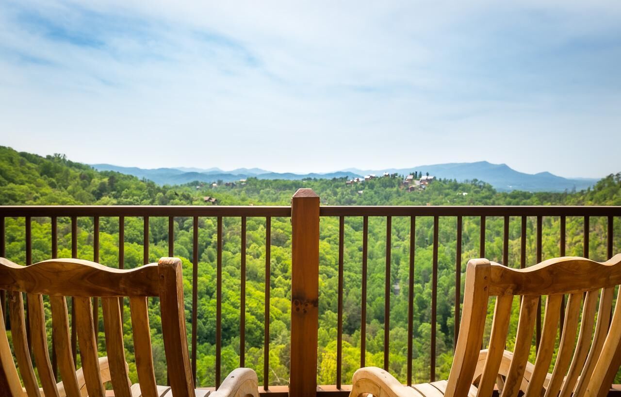 Eine Holzterrasse mit zwei Stühlen, die auf eine üppige, grüne Landschaft mit Bergen in der Ferne blickt.