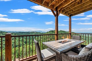 A wooden deck with a table and chairs, overlooking a lush green landscape. - Hidden Heaven (Sevierville)