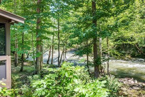 A forested area with a river, a wooden structure, and dense greenery. - River Lodge (Sevierville)