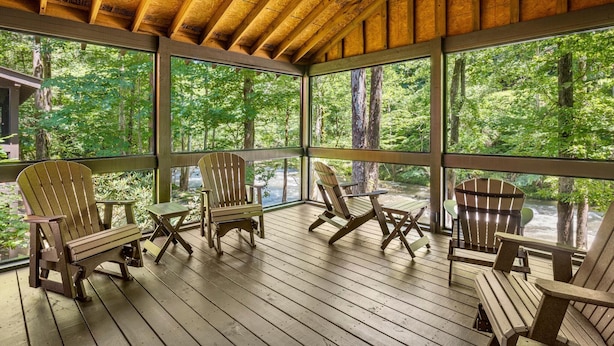 En overdækket veranda med Adirondack-stole og udsigt til et skovområde.