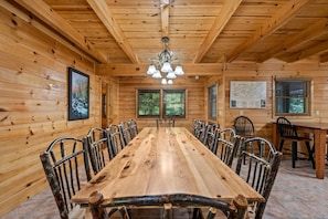 Ein Holzinterieur mit einem langen Esstisch, Metallstühlen, einer Deckenleuchte und gerahmten Bildern an den Wänden.