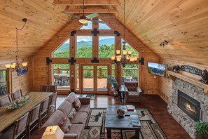 Ein geräumiges Loft mit hohen Decken, Holzwänden, einem Kamin, einem Essbereich und großen Fenstern mit Blick auf die Berge.