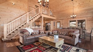 A log cabin interior with a wooden staircase, leather sofas, a coffee table, and a chandelier. - Smoky's Grand View (Gatlinburg)