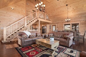 Ein Holzblockhaus-Interieur mit einer Holztreppe, Ledersofas, einem Couchtisch und einem Kronleuchter.