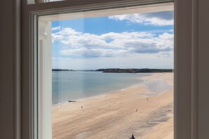 Blick auf einen Strand durch ein Fenster mit blauem Himmel und ruhiger See.