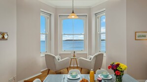 Een eethoek met een tafel gedekt voor twee personen, een bloevas en uitzicht op zee.