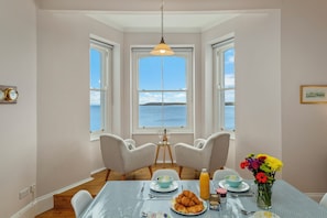 Ein Essbereich mit Tisch für zwei Personen, einer Blumenvase und Blick auf das Meer.
