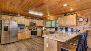 A kitchen with wooden cabinets, stainless steel appliances, a granite countertop, and a bar area with stools. - Dancing Bear Lodge (Gatlinburg)