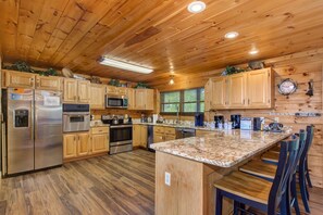 A kitchen with wooden cabinets, stainless steel appliances, a granite countertop, and a bar area with stools. - Dancing Bear Lodge (Gatlinburg)