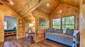 A cabin with a wooden interior, a bed, a sofa, a lamp, a fire extinguisher, and a window with blinds. - Dancing Bear Lodge (Gatlinburg)