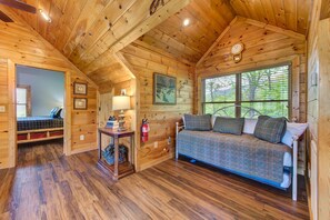 A cabin with a wooden interior, a bed, a sofa, a lamp, a fire extinguisher, and a window with blinds. - Dancing Bear Lodge (Gatlinburg)