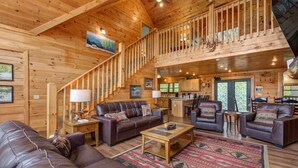 A spacious log cabin interior with a living area, a staircase, and a kitchen. - Dancing Bear Lodge (Gatlinburg)