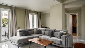 A modern living room with a grey sectional sofa, a wooden coffee table, and a sliding glass door leading to an outdoor area. - Comme a la maison (Alepou)