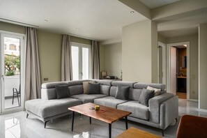 A modern living room with a grey sectional sofa, a wooden coffee table, and a sliding glass door leading to an outdoor area. - Comme a la maison (Alepou)