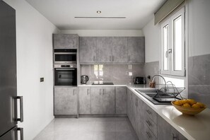 A modern kitchen with grey cabinets, a stainless steel refrigerator, an oven, and a sink. - Comme a la maison (Alepou)