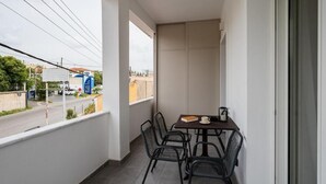 A balcony with a table and chairs, a view of the street, and a building with signage in the background. - Comme a la maison (Alepou)