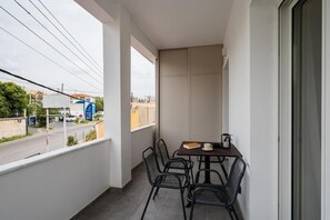 A balcony with a table and chairs, a view of the street, and a building with signage in the background. - Comme a la maison (Alepou)