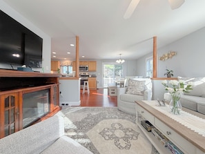 A modern living room with a television, a sofa, a coffee table, and a kitchen in the background. - Spacious 4BR Portland Retreat 4 King Beds + BBQ (Westbrook)