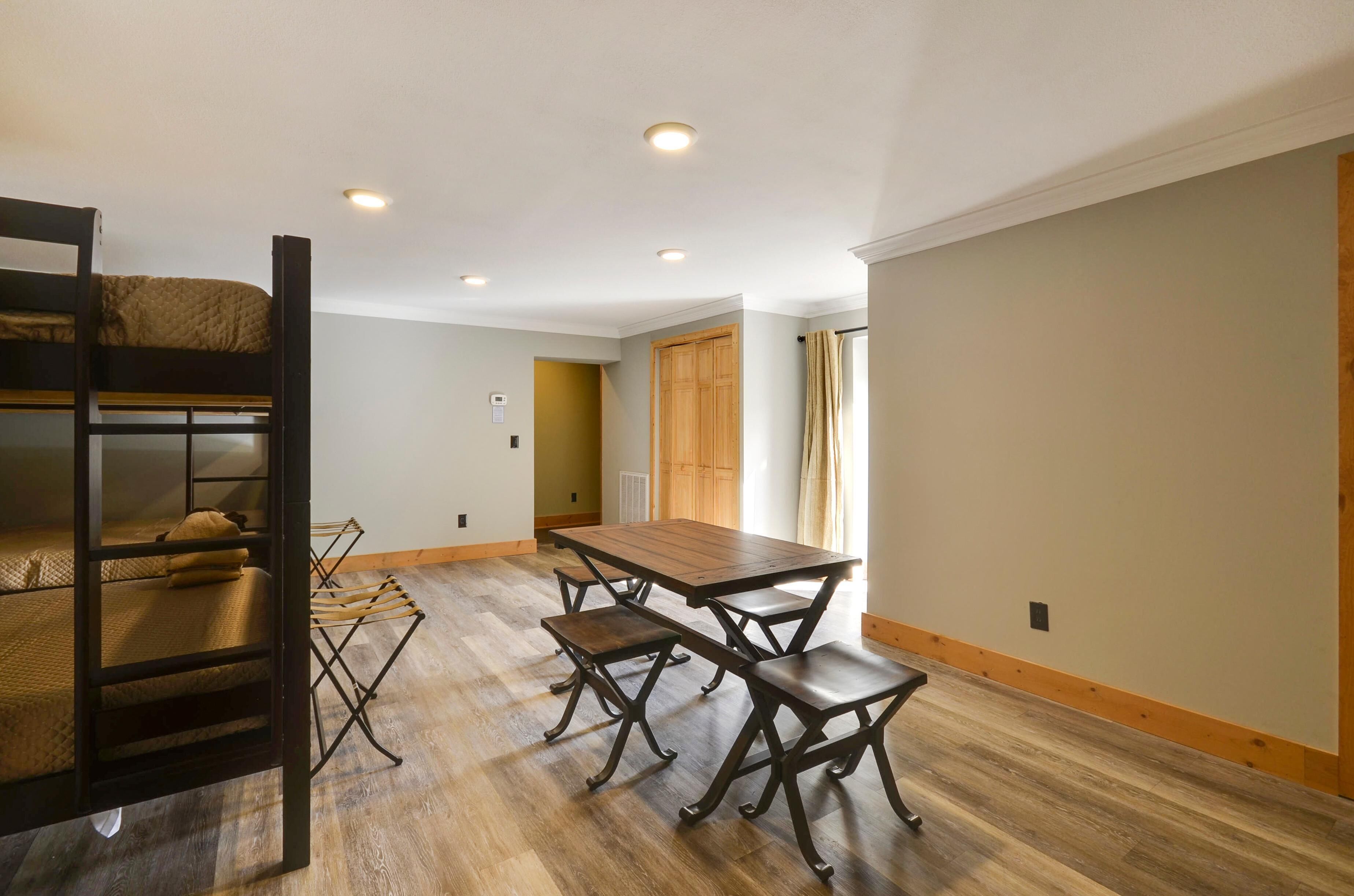 A room with a bunk bed, a wooden dining table with benches, and a wooden floor.