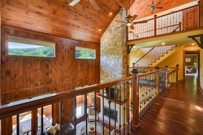 Un intérieur en bois avec une cheminée en pierre, un escalier et un balcon offrant une vue sur l’extérieur.