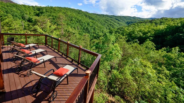 Eine Terrasse mit Liegestühlen und Geländer mit Blick auf ein bewaldetes Tal.