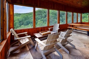A wooden cabin with large windows, outdoor seating, and a view of a forested area. - Mossy Brook Lodge (Sevierville)