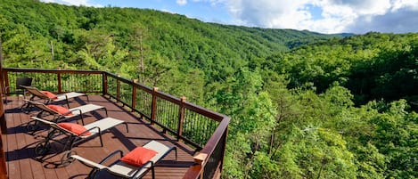 A deck with lounge chairs and a railing overlooking a forested valley.