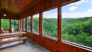 Eine Holzhütte mit großen Fenstern mit Blick auf ein bewaldetes Tal.