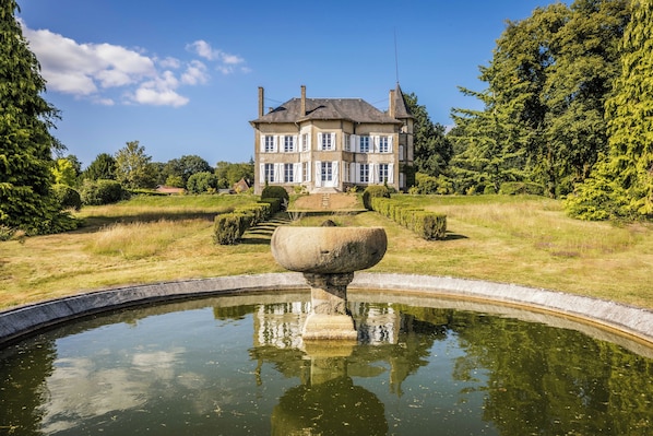 A large, multi-story building with a symmetrical facade, a central entrance, and a surrounding garden with a pond.