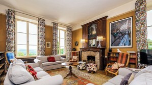 Een ruime woonkamer met een open haard, een groot raam en uitzicht op de omgeving.
