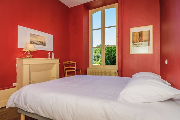 A bedroom with a bed, a chair, a radiator, and a window with a view of greenery. - Le Petit Château: a cozy oasis in the heart of the Limousin countryside (Vicq-sur-Breuilh)