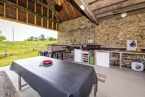 Une cuisine extérieure avec des murs en pierre, un four en briques et une table recouverte d’une nappe noire.