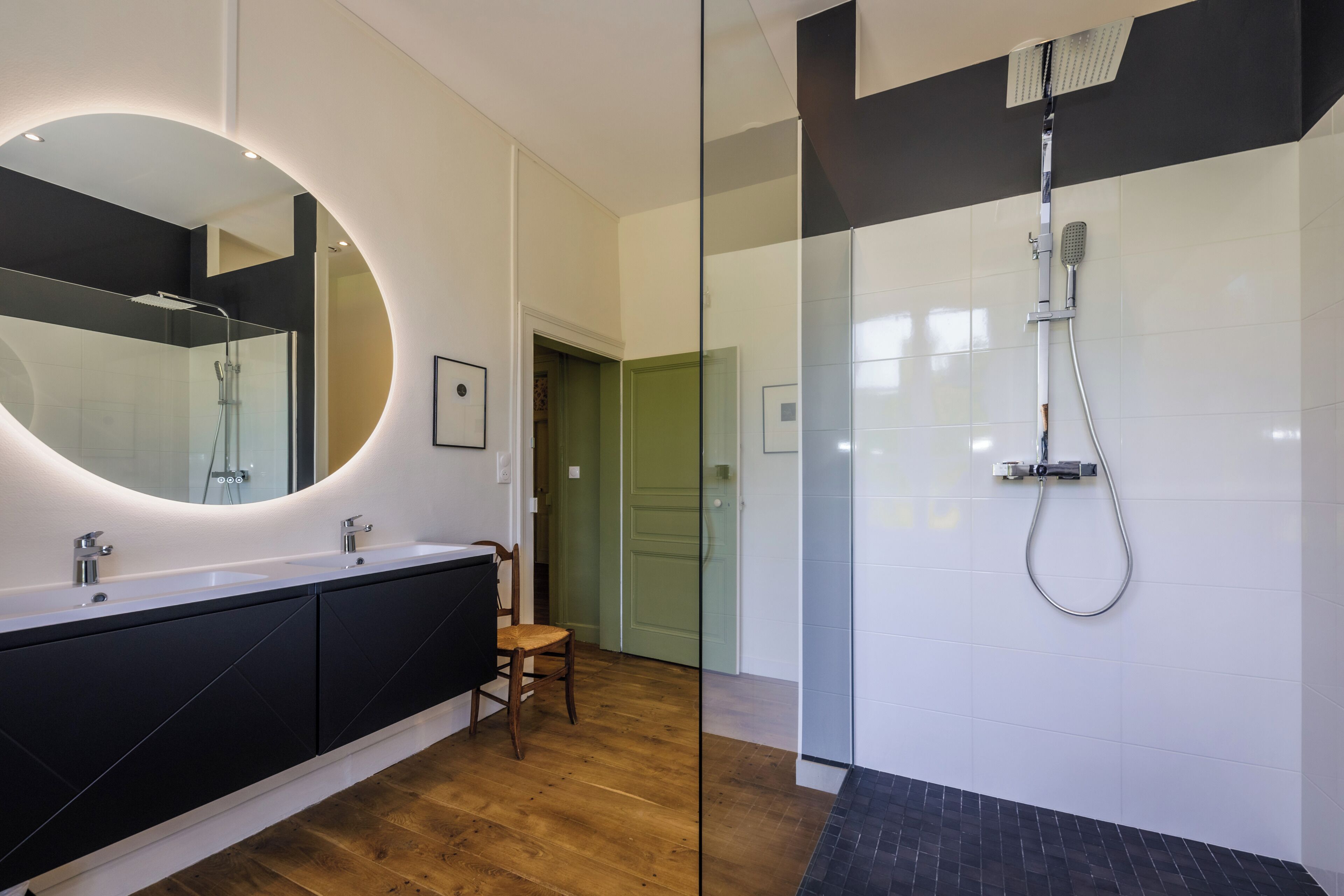 Un bagno moderno con uno specchio grande, una doccia e un pavimento in legno.