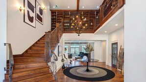 A wooden staircase with a railing, a chandelier, a round table with a rug, and a bookshelf in the background. - Haven and Hearth (Gatlinburg)