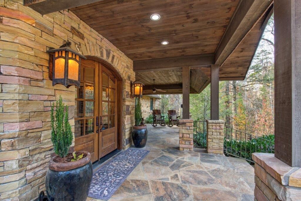 A stone exterior with a wooden porch, a door with glass panels, and two potted plants.