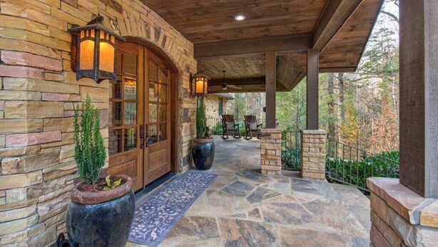 A stone exterior with a wooden porch, a door with glass panels, and two potted plants. - Haven and Hearth (Gatlinburg)