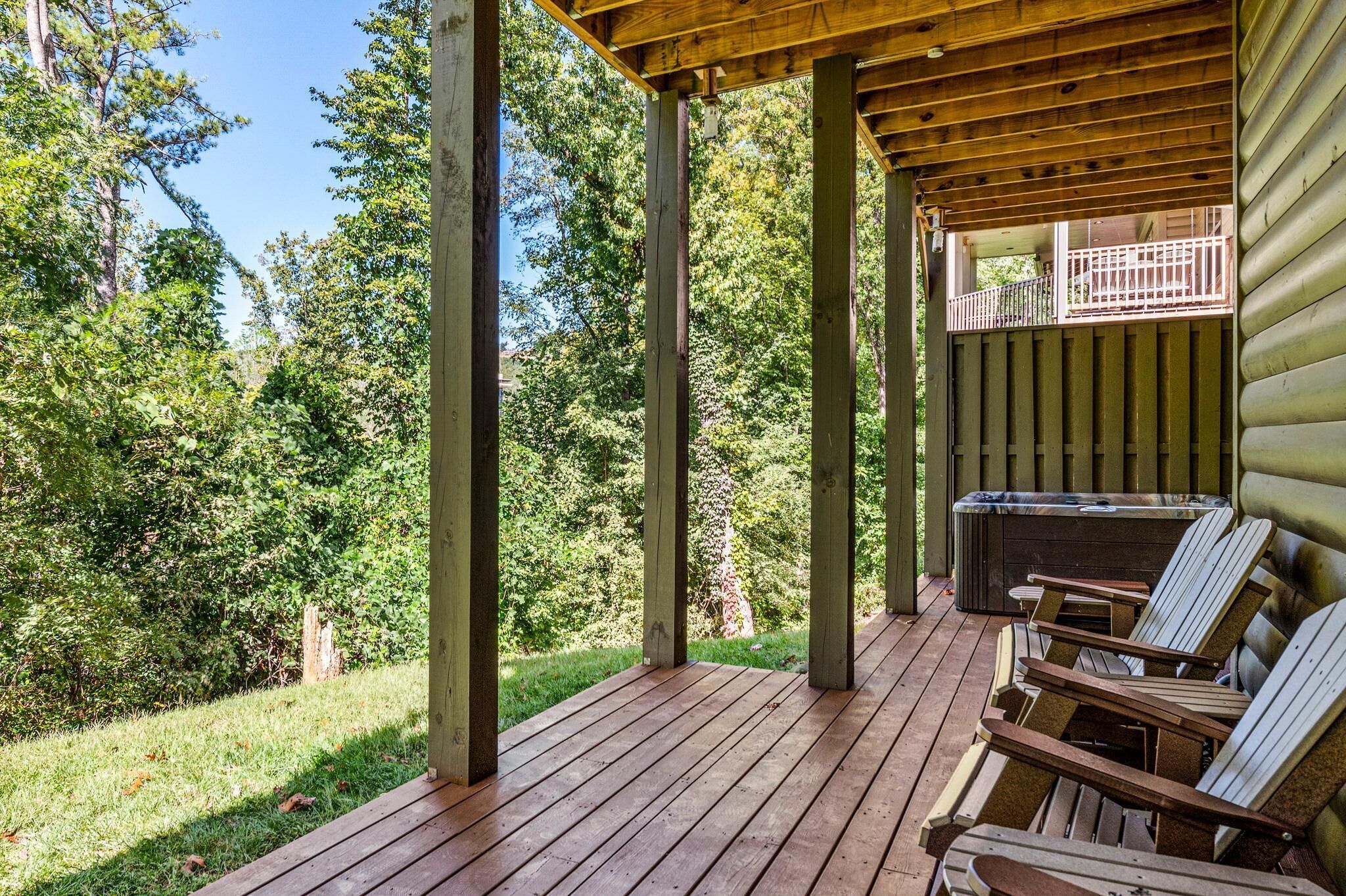 Una terraza cubierta con sillas de madera, un jacuzzi y vistas a un área boscosa.