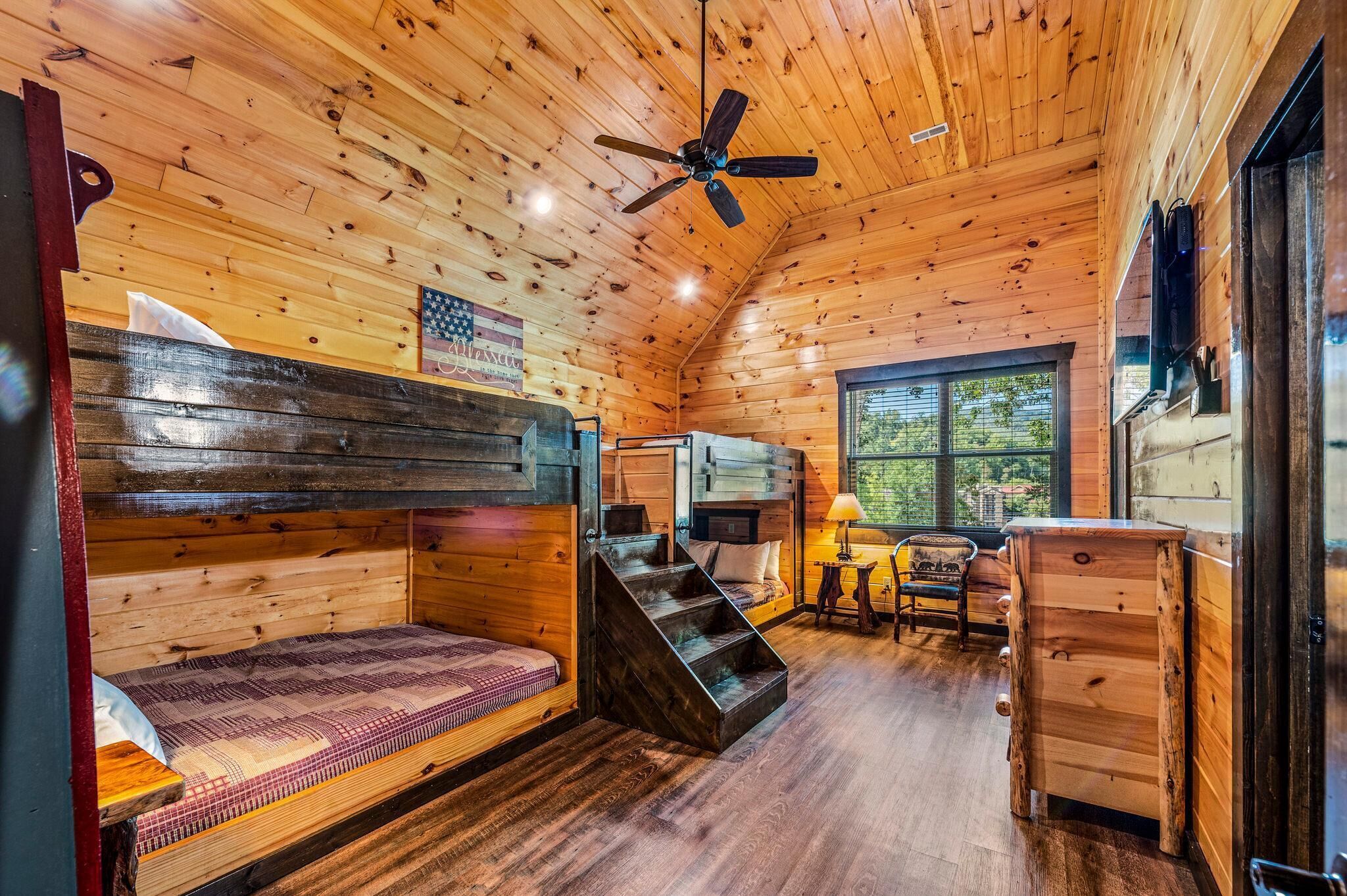 A cabin interior with wooden walls, a bunk bed, a desk, and a window.
