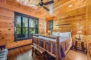 A wooden cabin room with a bed, bench, ceiling fan, and two windows. - The Mighty Crabapple Manor (Gatlinburg)