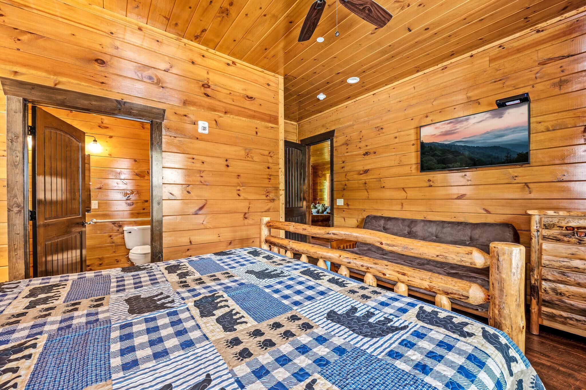 A wooden cabin interior with a bed, a sofa, a television, and a bathroom.
