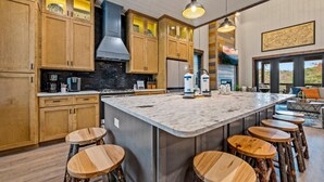 A modern kitchen with wooden cabinets, a large island with stools, and a view to the outside. - Splash Villa (Pigeon Forge)